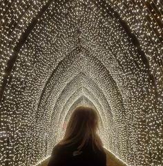 a woman walking through a tunnel covered in lights