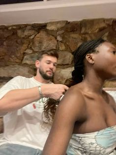 a woman is getting her hair styled by a man in front of a stone wall