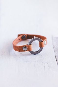 a brown leather bracelet with two metal rings on it's end, sitting on a white surface