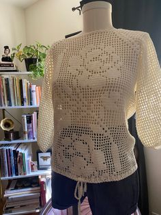 a crocheted top on a mannequin in front of a bookshelf