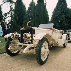 an antique car parked on the side of a dirt road with people standing around it