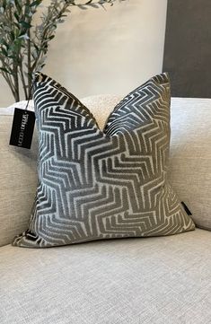 a white and black pillow sitting on top of a couch next to a potted plant