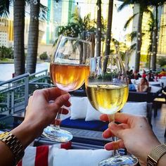 two people toasting with wine glasses in front of palm trees on a balcony overlooking the ocean