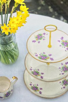 yellow flowers are in a vase next to three plates and a teapot on a table