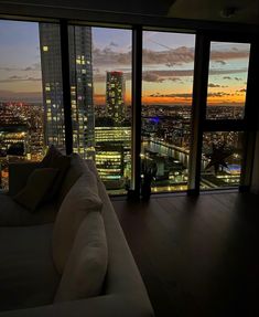 a living room filled with furniture and large windows overlooking the city at sunset or dawn