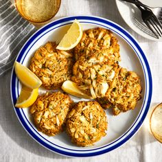 a white plate topped with crab cakes next to lemon wedges and silverware on top of a table