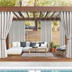 an outdoor living area next to a swimming pool with curtains and furniture on the deck