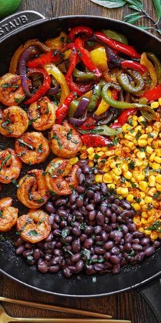 a skillet filled with beans, peppers and corn on top of a wooden table