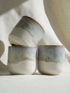 three white and blue cups sitting next to each other on top of a tablecloth