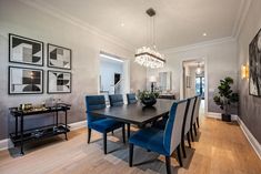 a dining room table with blue chairs and pictures on the wall in front of it