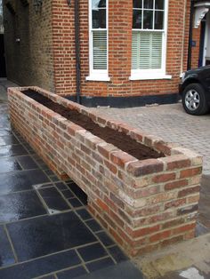 a brick bench sitting in front of a building on a cobblestone street with a car parked next to it