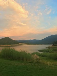 a large body of water sitting next to a lush green field under a cloudy sky