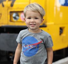 a little boy that is standing in front of a yellow truck and smiling at the camera