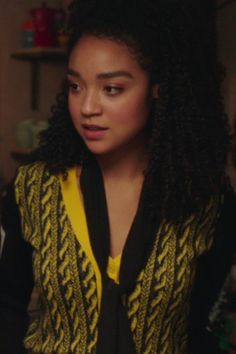 a young woman with curly hair wearing a yellow and black sweater is looking at the camera