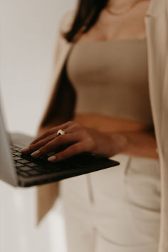 a woman holding a laptop computer in her right hand and wearing a ring on the other hand