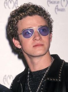 a young man with curly hair wearing sunglasses and a black leather jacket is posing for the camera