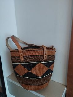 Geometrical earth tone sisal tote bag. Unique and stylish colorful sisal kiondo bag with stitched leather straps, pocket lining and zipper. Patterns and sizes slightly vary because weaving and stiching is done by hand. Ideal as a beach bag, shopping basket, market basket or storage basket. This unique tote bag is handmade by a group of ladies in a remote rural village in Machakos, Kenya. Do not clean with brush or water. If the bag gets wet, please dry to avoid dampness.  Leather type used is bo Brown Box Bag With Handles For Shopping, Woven Handheld Bag For Daily Use, Handheld Woven Bag For Daily Use, Brown Bucket Shoulder Bag With Handles, Woven Double Handle Shoulder Bag For Shopping, Brown Rectangular Bag With Leather Handles, Brown Rectangular Bags With Leather Handles, Brown Square Satchel With Handles, Rectangular Brown Bucket Bag For Shopping