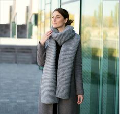 a woman standing in front of a building wearing a gray coat and scarf over her shoulders