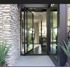 an entry way leading to a house with glass doors and large plants on either side