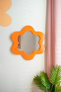 an orange mirror on the wall next to a potted plant