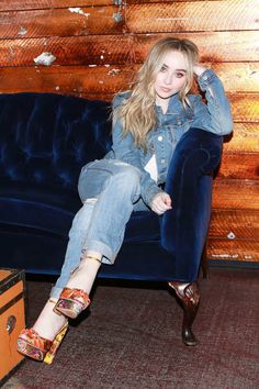 a young woman sitting on top of a blue couch next to a suitcase and wooden wall