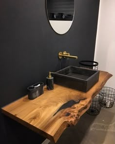 a bathroom with a wooden counter top and black walls, along with a round mirror on the wall