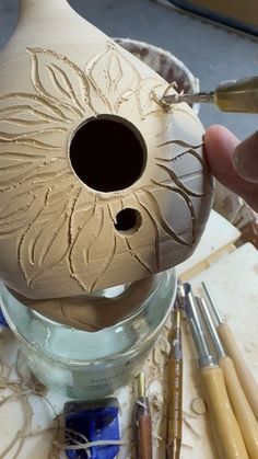 a person is painting a vase on a table with paintbrushes and crayons