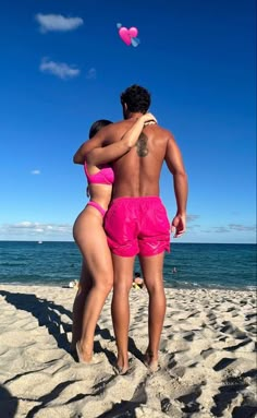 a man and woman in pink swimsuits standing on the beach facing each other