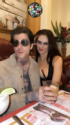 a man and woman sitting at a table with drinks in front of them, posing for the camera