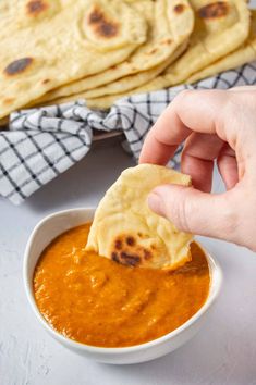 a person dipping some food into a bowl with pita bread in the back ground