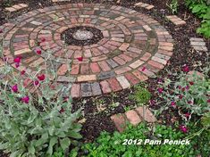 a circular brick garden path surrounded by flowers and greenery in the middle of a flower bed