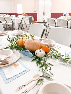 a table set for thanksgiving dinner with pumpkins and greenery on the centerpiece