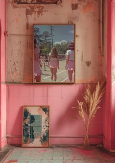 a pink room with two framed pictures on the wall and a potted plant next to it