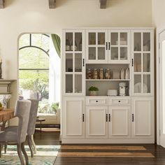 a dining room table and chairs in front of a white china cabinet with glass doors