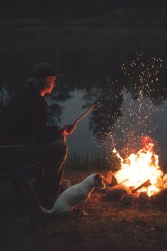 a man sitting in front of a campfire next to a white dog and cat