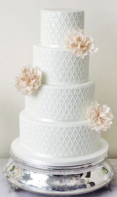 a three tiered white wedding cake with flowers on the side and candles next to it