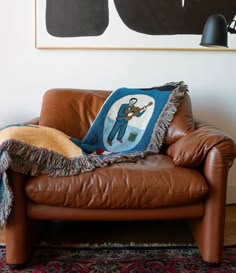 a brown leather couch with a blanket on it in front of a black and white painting