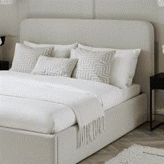 a bed with white linens and pillows in a neutral bedroom, along with two nightstands