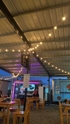 the inside of a restaurant with wooden tables and chairs, lights strung from the ceiling