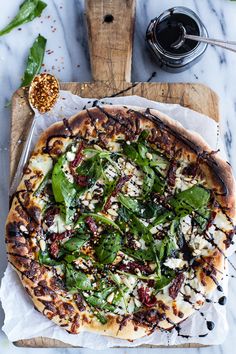 a pizza with spinach, cheese and other toppings on it sitting on wax paper