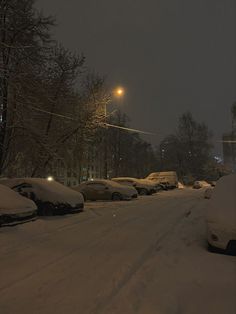 cars are parked on the side of a snowy road at night time, with street lights in the distance