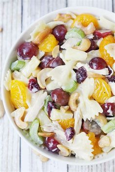 a white bowl filled with fruit salad on top of a wooden table next to cashews