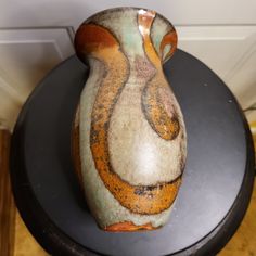 a ceramic vase sitting on top of a black table next to a white and brown wall