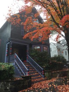 a house with fall leaves on the ground and stairs leading up to it's front door