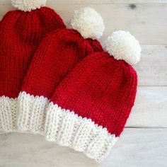 two red and white knitted hats with pom - poms sitting on top of each other