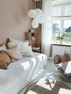 a bedroom with pink walls and white bedding, pillows and rugs on the floor