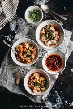 three bowls of food sitting on top of a newspaper next to spoons and glasses