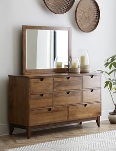 a wooden dresser with two baskets hanging on the wall above it and a large mirror