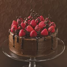 a chocolate cake topped with strawberries on top of a glass plate next to a brown wall