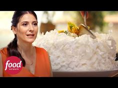 a woman standing in front of a large white cake with flowers on it and the words food network